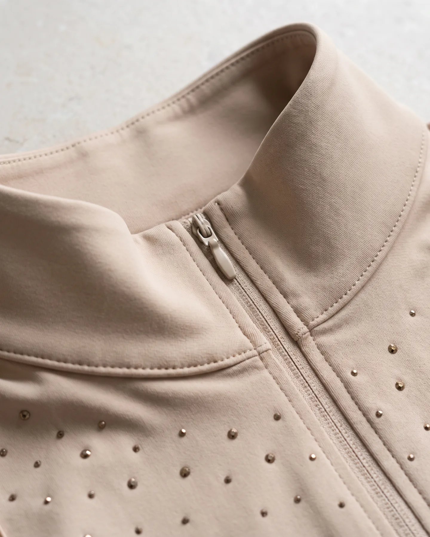 Col montant et patte zippée d’une chemise de concours beige semée de strass