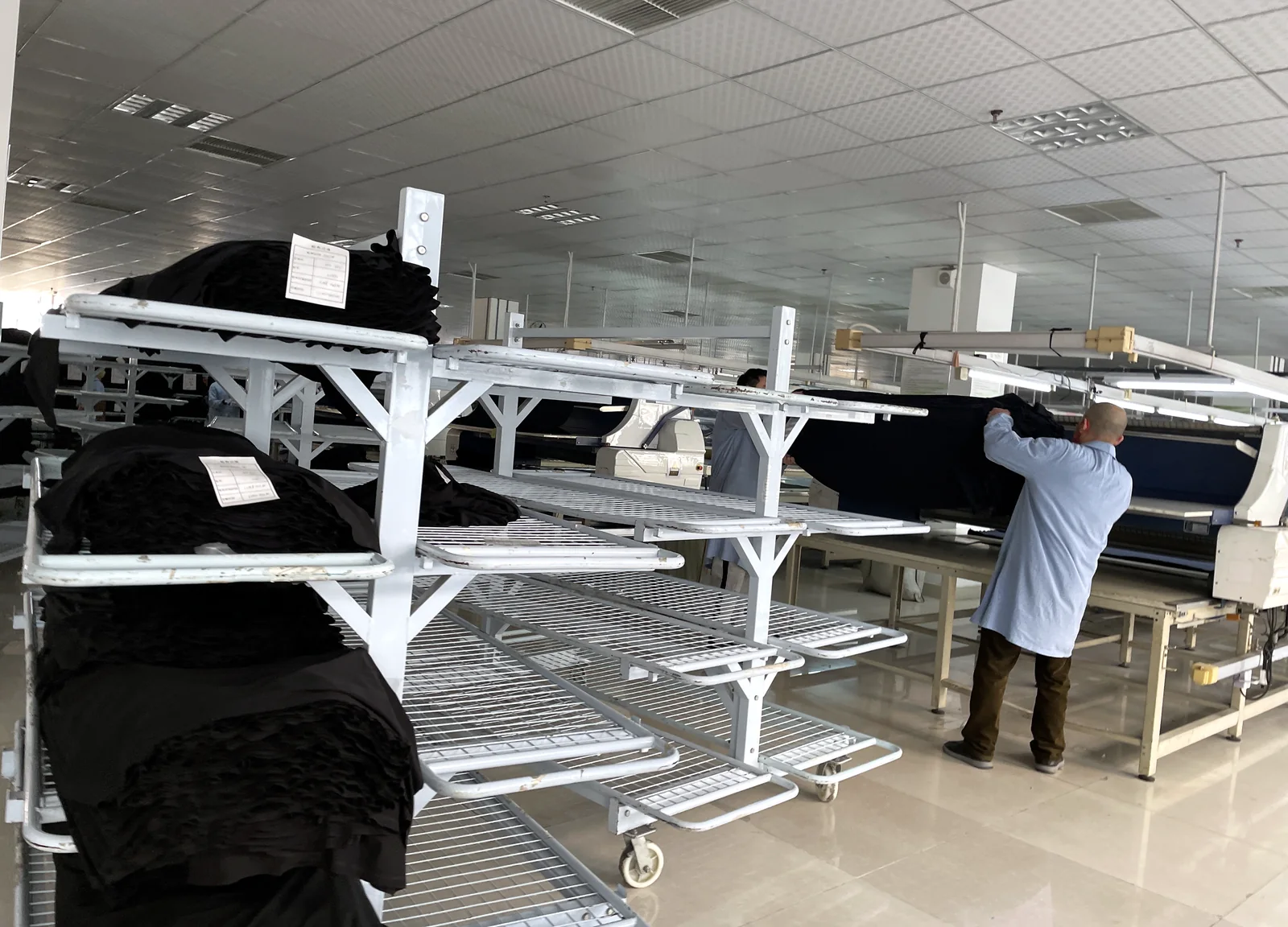 Préparation du tissu avant la coupe, rouleaux sur chariots et table d’étalage